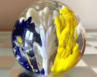 May include: A clear glass paperweight with blue, white, and yellow glass flowers inside.