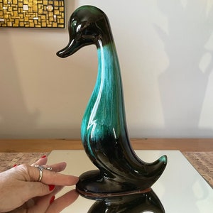 May include: A ceramic duck ornament with a glossy finish. The duck has a long, curved neck and a rounded base. The color transitions from black to teal green. The figurine is approximately 30 cm tall.
