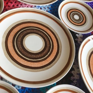 Op de afbeelding: Set van zes witte keramische dinerborden met een concentrisch cirkelontwerp in tinten bruin, beige en oranje.