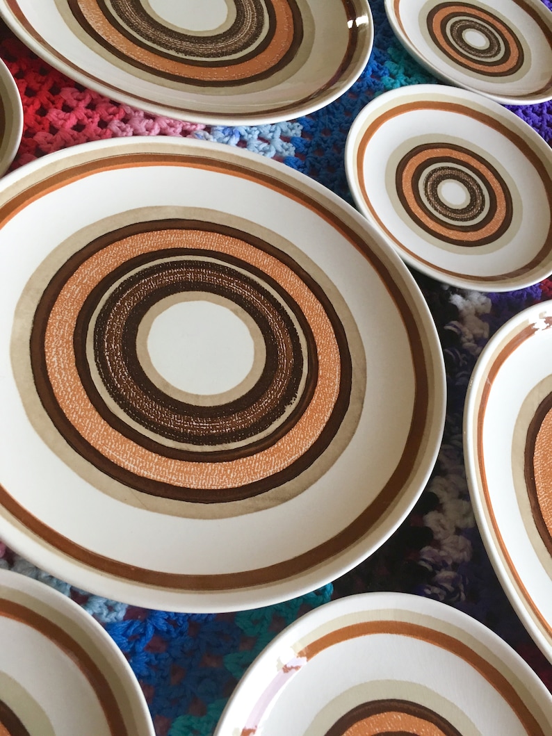Op de afbeelding: Set van zes witte keramische dinerborden met een concentrisch cirkelontwerp in tinten bruin, beige en oranje.