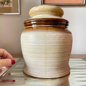 May include: A ceramic jar with a brown and white striped design. The jar has a lid with a rounded top.