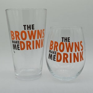 May include: Two clear glass drinking glasses with the text "The Browns Make Me Drink" printed in orange and black on each glass.