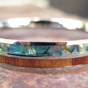 May include: A silver ring with a band of wood and a thin band of iridescent abalone shell.