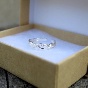 May include: A silver toe ring with a floral design. The ring is in a small, brown box with white lining.