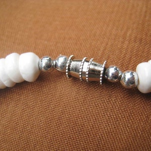 May include: White bead bracelet with a silver clasp. The bracelet is made of small, round beads that are strung together on a silver chain. The clasp is a simple, silver loop that is easy to open and close.