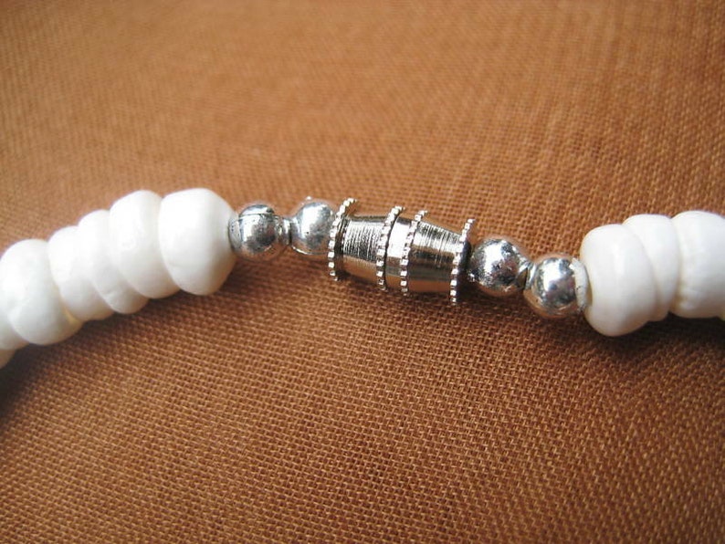 May include: White bead bracelet with a silver clasp. The bracelet is made of small, round beads that are strung together on a silver chain. The clasp is a simple, silver loop that is easy to open and close.