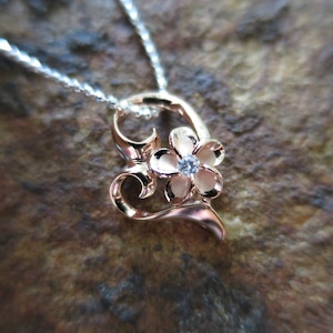 Puede incluir: Un collar con un colgante en forma de coraz&oacute;n de oro rosa, adornado con un delicado dise&ntilde;o floral y una sola piedra preciosa transparente en el centro.