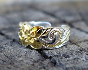 May include: A silver toe ring with a gold flower design. The ring is set on a textured gray surface.