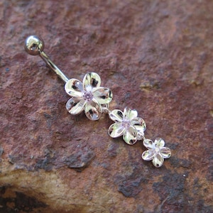 May include: Silver belly button ring with three dangling flower charms. Each flower has a pink rhinestone in the center.