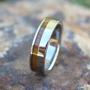 May include: A silver band with a thin strip of wood inlay. The band is polished and has a smooth finish.