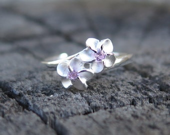 May include: A silver ring with two flower designs, each with a small pink gemstone in the center.