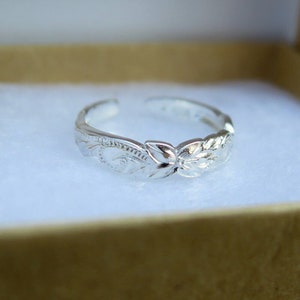 May include: A silver toe ring with a floral design. The ring is adjustable and has a polished finish.