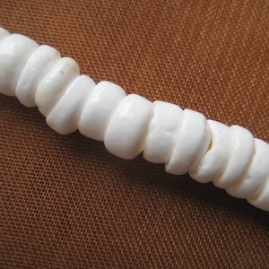 May include: A white beaded necklace made of smooth, round beads. The beads are strung together on a white cord.