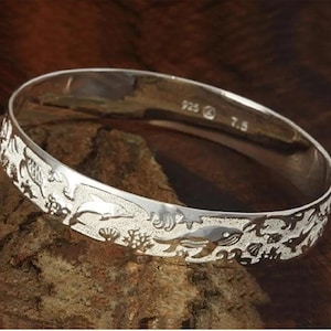 May include: A silver bangle bracelet featuring an intricate design of sea creatures, including dolphins, fish, and coral. The bracelet is marked "925" and "7.5".