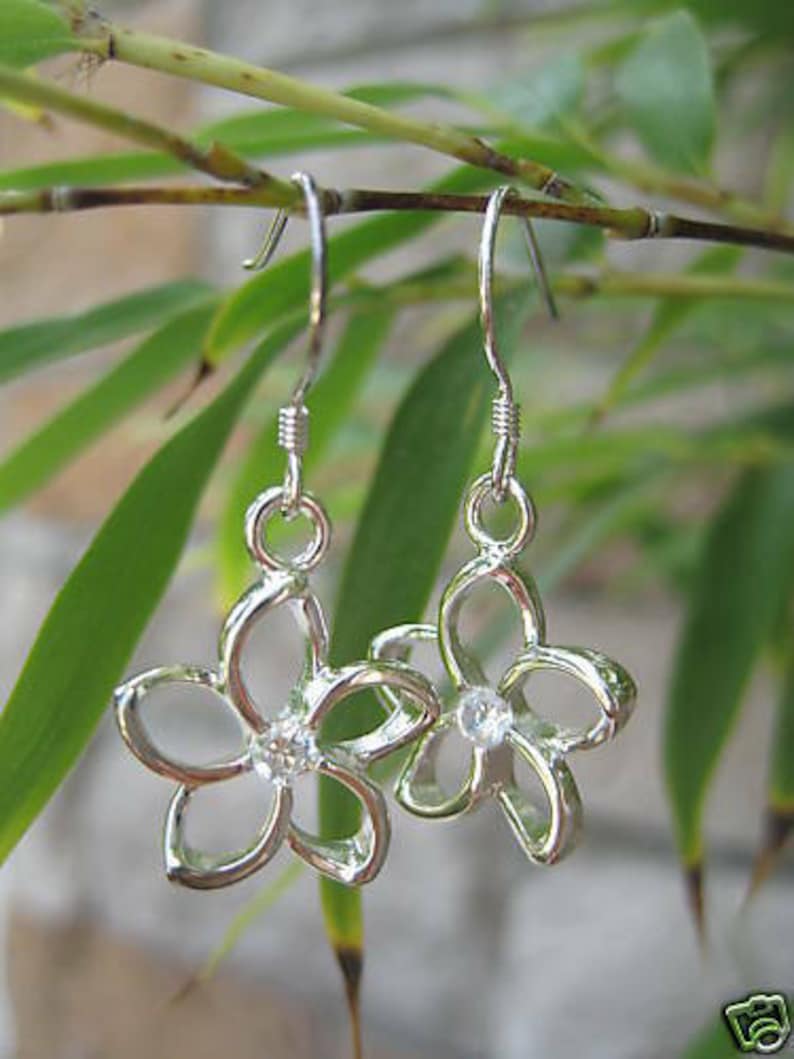 Pu&ograve; includere: Orecchini pendenti in argento con un design a forma di fiore e un cristallo trasparente al centro di ogni fiore.