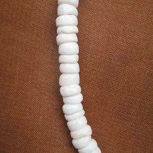 May include: A white shell necklace made of small, round beads. The necklace is strung together with a simple knot.