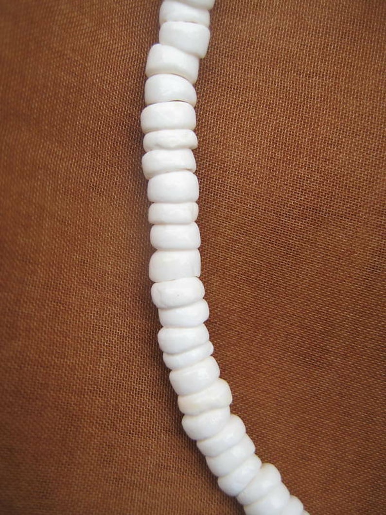 May include: A white shell necklace made of small, round beads. The necklace is strung together with a simple knot.