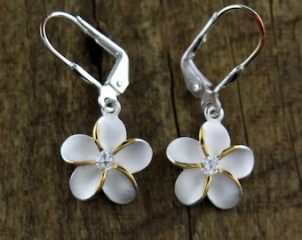May include: A pair of silver dangle earrings with white flower charms and gold accents. Each flower has a clear rhinestone in the centre.