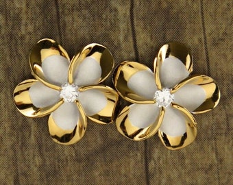 May include: A pair of gold and white flower-shaped earrings with a clear rhinestone in the centre of each flower.