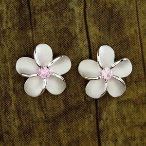 Può includere: Un paio di orecchini a forma di fiore argentati con centri di cristallo rosa. I fiori sono bianchi con accenti argentati.