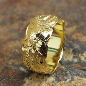 Puede incluir: Un anillo de oro con un diseño floral. El anillo está grabado con un patrón de flores y tiene un acabado liso y pulido.