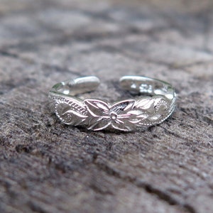 May include: A silver toe ring with a floral design. The ring is adjustable and has a delicate, intricate pattern.