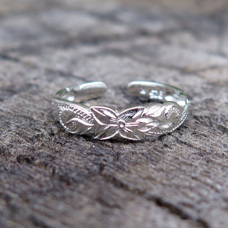 May include: A silver toe ring with a floral design. The ring is adjustable and has a delicate, intricate pattern.