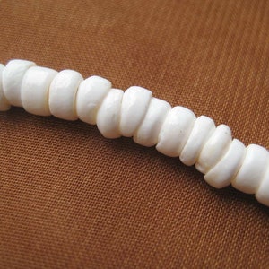 May include: A strand of white shell beads, strung together to form a necklace or bracelet. The beads are smooth and round, with a natural, organic look.