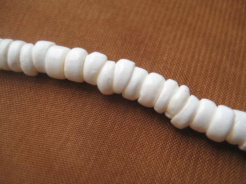May include: A strand of white shell beads, strung together to form a necklace or bracelet. The beads are smooth and round, with a natural, organic look.