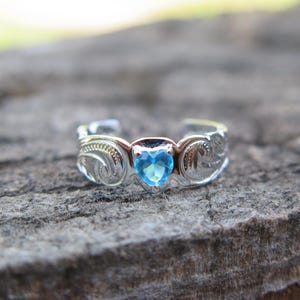 May include: A silver toe ring with a blue heart-shaped gemstone and intricate scrollwork design.