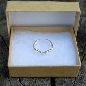 May include: A silver toe ring with a delicate floral design, displayed in a brown box with white lining.