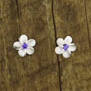 Può includere: Un paio di orecchini d'argento a forma di fiore con centri di cristallo viola.