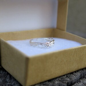 May include: A silver toe ring with a floral design. The ring is in a small, brown box with white lining.