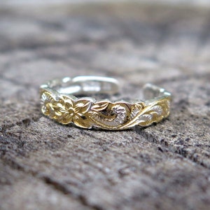 Pode incluir: Um anel de dedo do pé de prata com um design floral dourado. O anel é ajustável e tem um padrão delicado e intrincado.