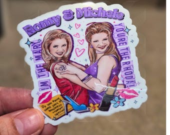 May include: A sticker featuring a cartoon illustration of two women with the text "Romy & Michele" and "You're the Rhoda!" in pink and purple lettering. The women are wearing colorful outfits and are holding hands. The sticker also includes hearts and stars.