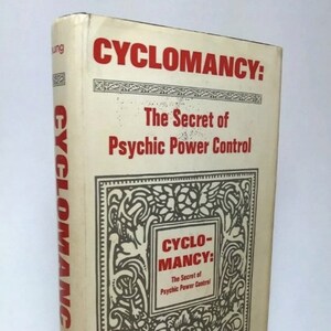 Może przedstawiać: Zabytkowa książka zatytułowana "CYCLOMANCY: The Secret of Psychic Power Control" autorstwa Franka Rudolpha Younga. Książka ma kremową okładkę z czerwonym i czarnym tekstem. Tytuł jest wyraźnie wyświetlany dużymi czerwonymi literami.