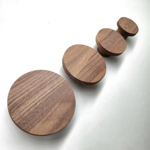 以下が含まれることがあります： さまざまなサイズの木製の丸いノブが4つセットになっています。ノブは、自然な木目模様のある濃い茶色の木でできています。