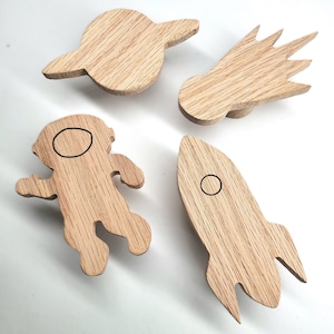 May include: Four wooden wall hooks shaped like a rocket, astronaut, comet, and planet. Each hook has a small circle cut out for hanging items.