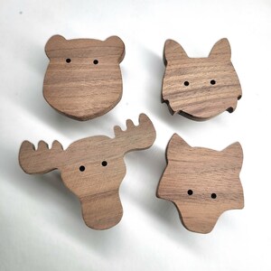 Könnte beinhalten: Vier Wanddekorationen aus Holz in Form eines Bären, Wolfs, Elchs und Fuchses. Die Stücke sind alle aus hellem braunem Holz gefertigt und haben schwarze Augen.