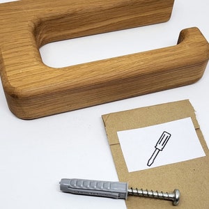 May include: A wooden toilet paper holder with a rectangular design. The holder is made of light brown wood and includes mounting hardware: screws and wall anchors. A small card with a screwdriver illustration is also included.