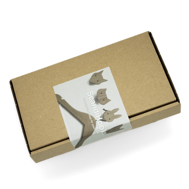 May include: A brown cardboard box with a white label featuring wooden animal-shaped hooks. The label reads "ScandiHooks" with a design for your home. The hooks are shaped like a fox, cat, and rabbit.