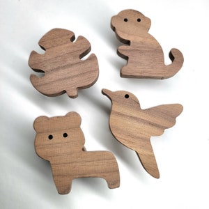 Puede incluir: Cuatro formas de madera recortadas de un pájaro, un mono, una hoja y un oso. Las formas son todas de madera marrón claro y tienen un acabado de madera natural.