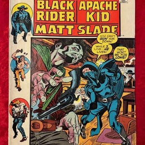 May include: A comic book cover featuring a black and white illustration of a cowboy with a gun and a blue and black illustration of a masked cowboy. The title of the comic is "Black Apache Rider Kid" and the subtitle is "Matt Slade". The text "Duel at Dawn!" is printed in red at the bottom of the cover.