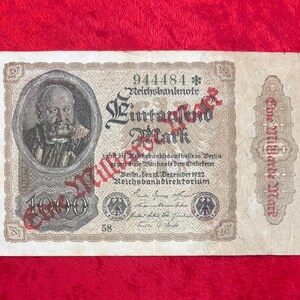 May include: A vintage 1000 Mark German banknote from 1922, featuring a portrait in a circular frame. The note has intricate designs, text in German, and a red seal. The text includes "Reichsbanknote" and "Eine Millarde Mark."