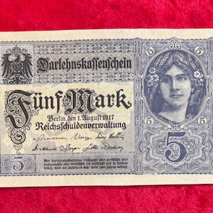 May include: A vintage German five Mark banknote from 1917, featuring intricate designs and text. The note displays an eagle emblem, the text "Darlehnskassenschein" and a portrait of a woman. The number "5" is prominently displayed.