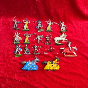 May include: A collection of toy knights and horses in various poses, set against a red background. The figures are painted in silver, yellow, blue, and red, with some holding weapons like swords, spears, and bows. The toys are on green bases.