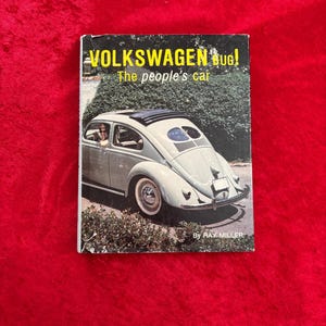 May include: A vintage book titled "VOLKSWAGEN bug! The people's car" featuring a light blue Volkswagen Beetle on the cover. The book is set against a red background. The cover includes the author's name, Ray Miller.