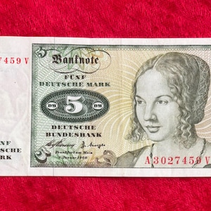 May include: A vintage five Deutsche Mark banknote from the Deutsche Bundesbank, featuring a portrait of a woman. The bill has green and gray details, with the number 5 prominently displayed. The text "FÜNF DEUTSCHE MARK" is visible.