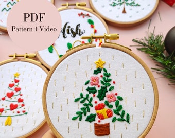 May include: A set of five embroidery hoop ornaments featuring Christmas-themed designs. The ornaments include a Christmas tree with red hearts, a Christmas tree with flowers, a Christmas tree with a star, a Christmas tree with a simple design, and a Christmas tree with the word "Wish" embroidered on it.