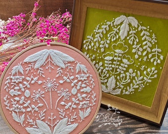 May include: Two embroidery hoops with floral designs. The hoop on the left is pink with white embroidery. The hoop on the right is green with white embroidery.